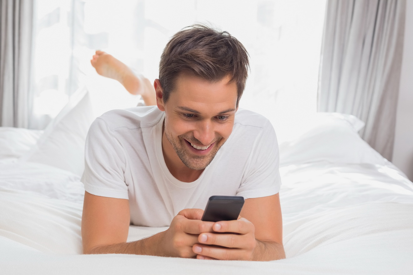 Young man text messaging in bed at home